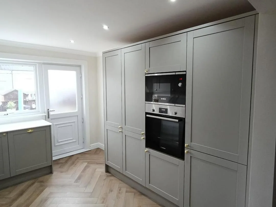Tall grey kitchen cabinetry with integrated ovens and herringbone flooring