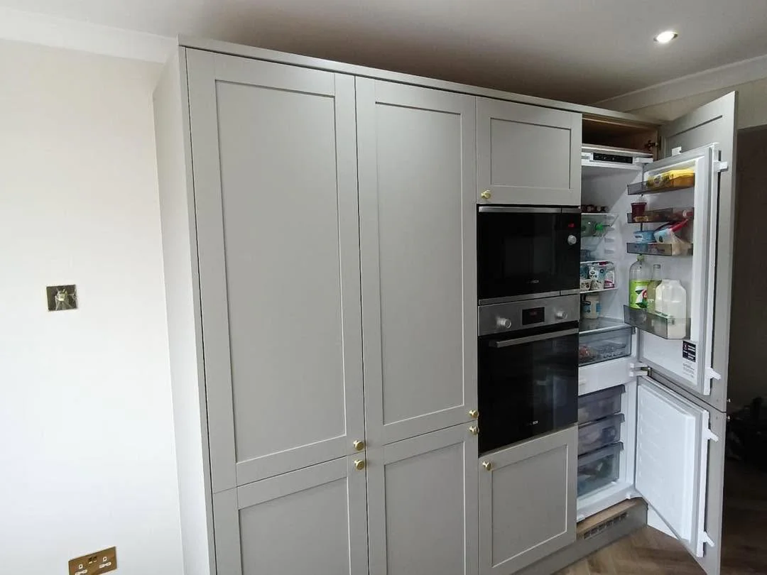 Integrated kitchen appliance wall with grey shaker cabinetry and brass handles