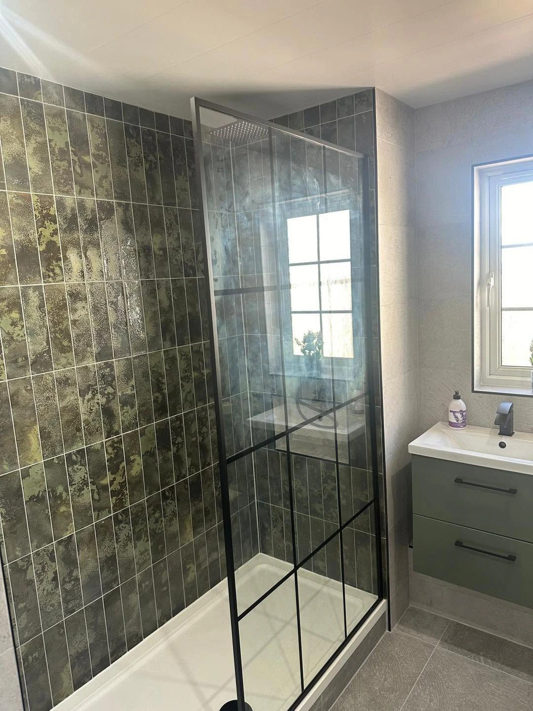 Green tiled shower enclosure beside a fitted vanity and window