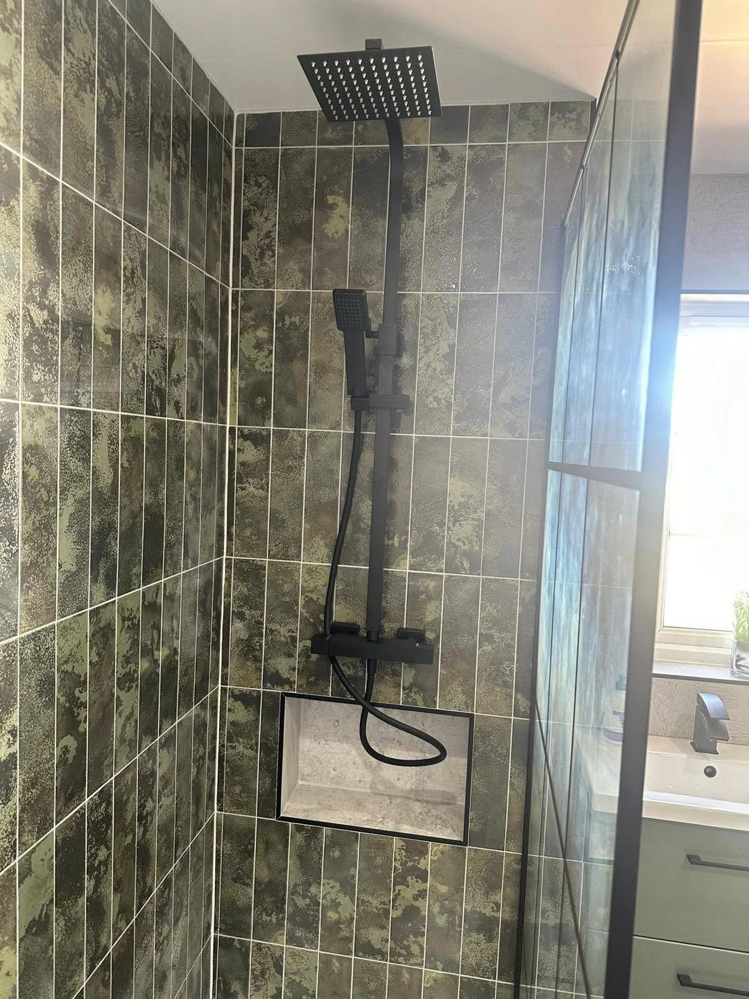 Black rainfall shower and recessed shelf against patterned green tiles
