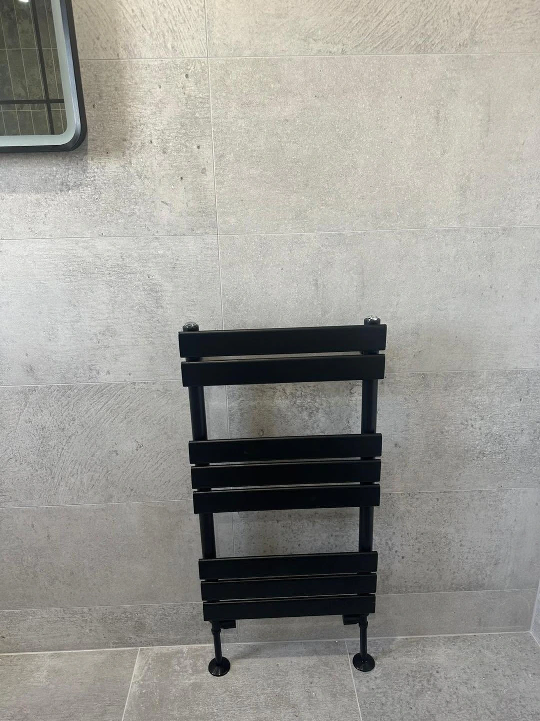 Black heated towel rail against large-format grey wall tiles