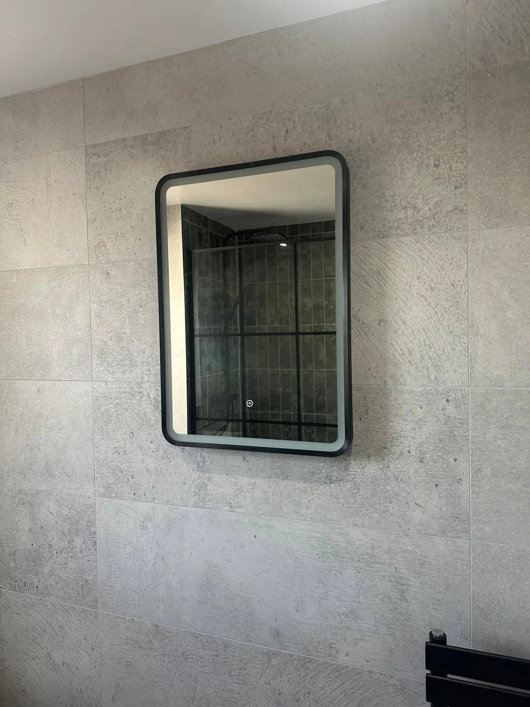 Illuminated black-framed mirror set against large-format grey wall tiles