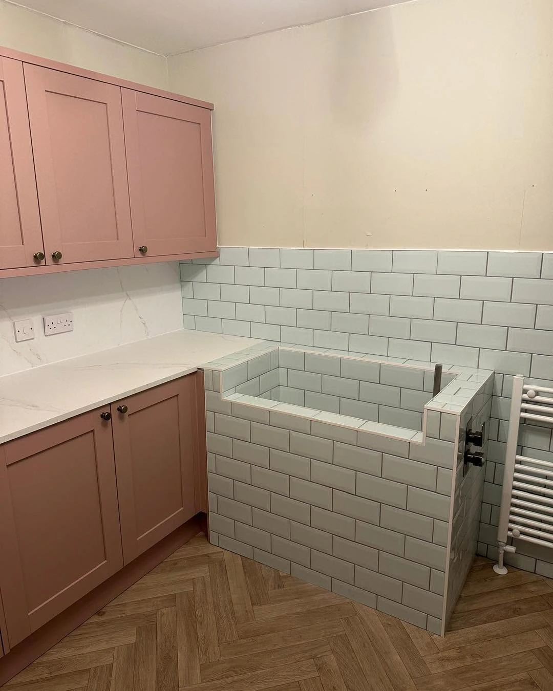 Utility room with blush fitted cabinetry, pale tiled wash area and herringbone flooring
