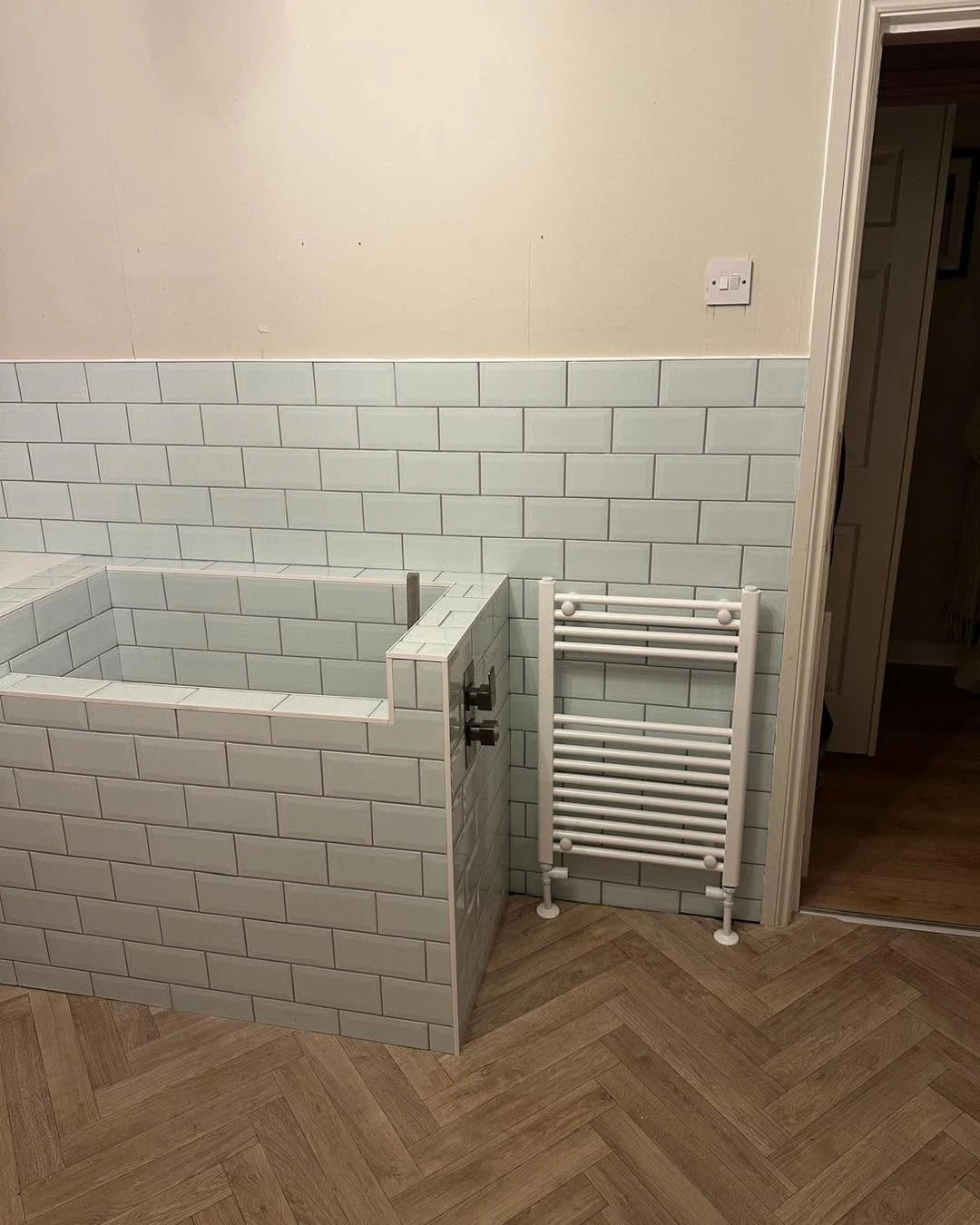 Pale tiled wash area beside a heated towel rail in the finished utility room