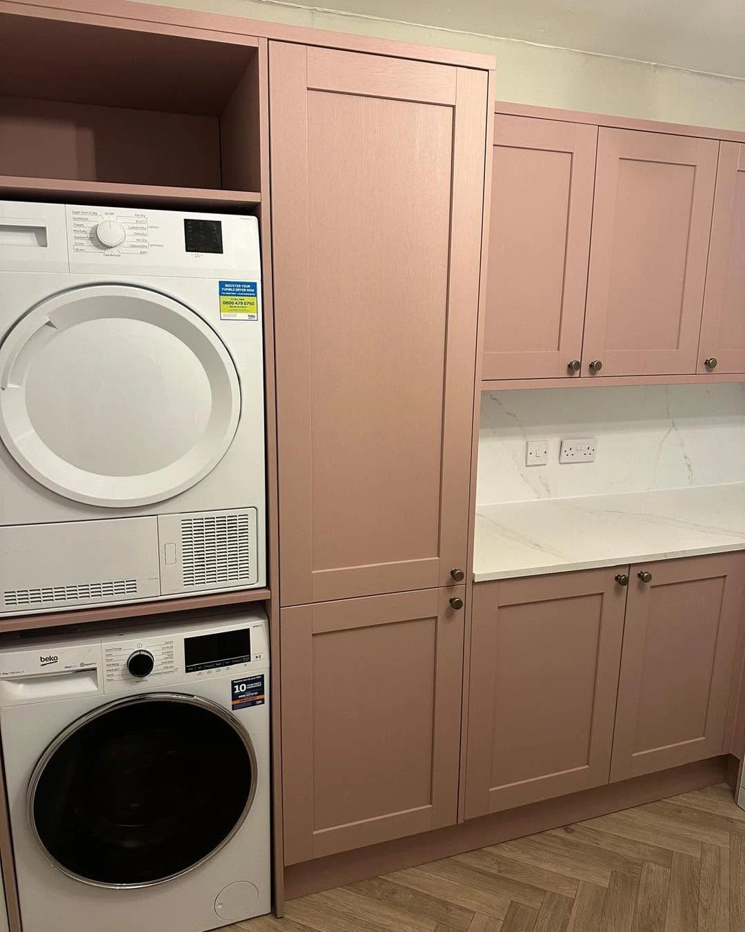 Stacked laundry appliances beside fitted blush utility room cabinetry
