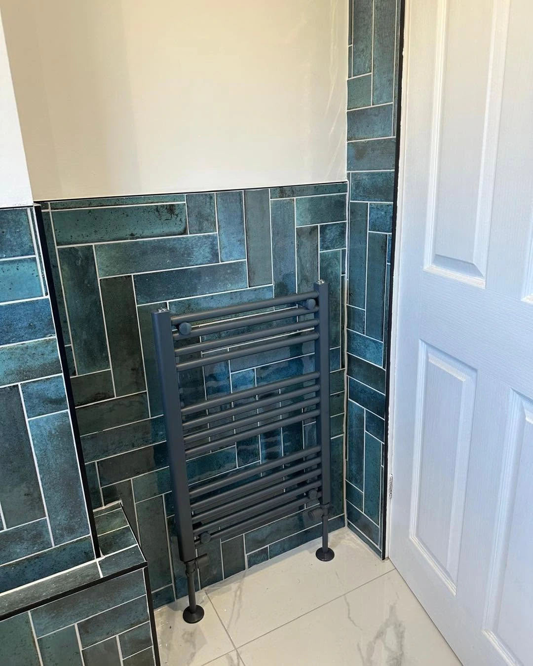 Dark heated towel rail against patterned teal wall tiles