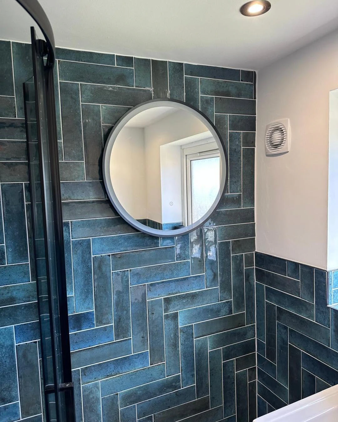 Round mirror set against patterned teal feature tiles beside the glazed shower