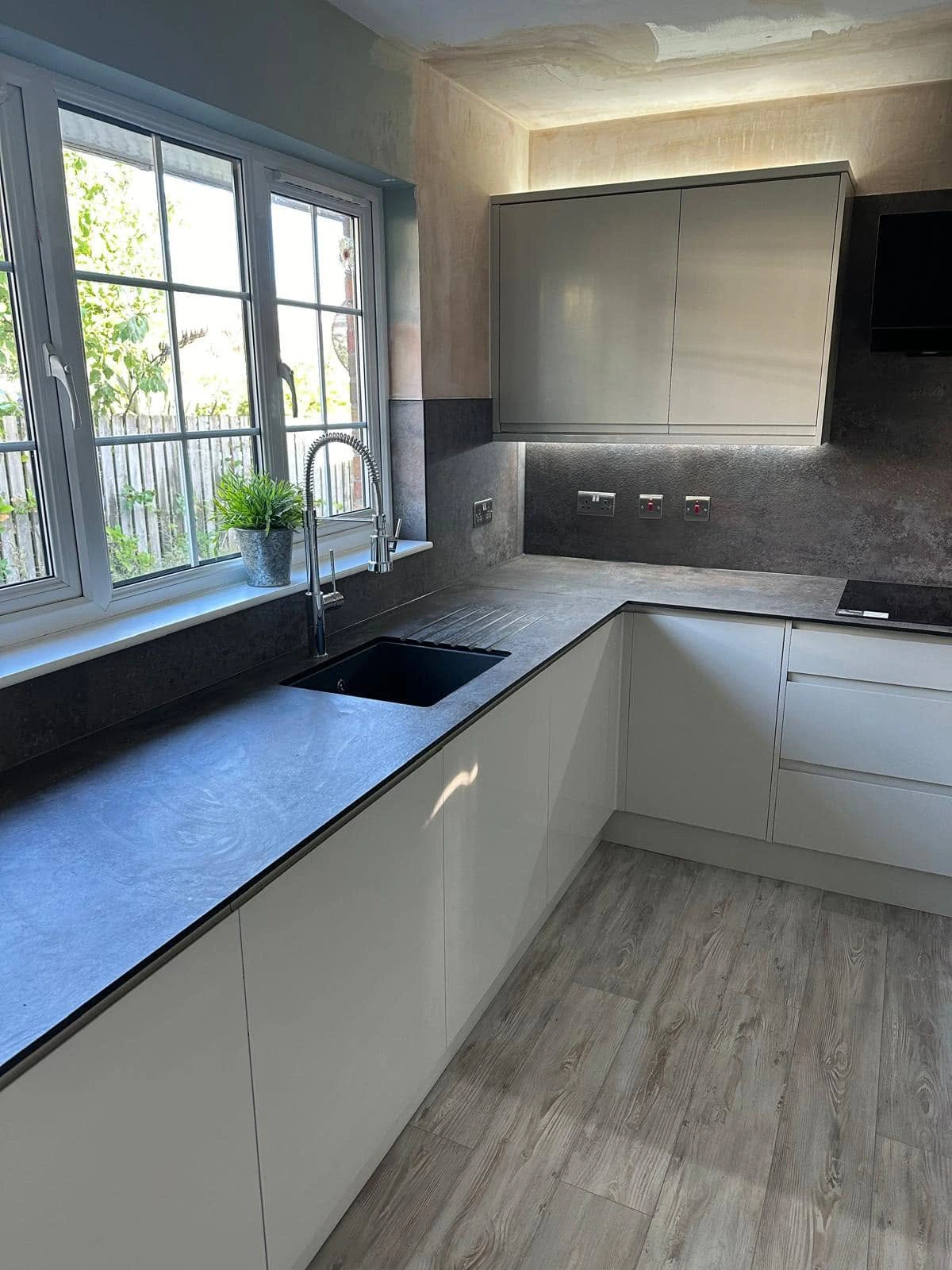 Contemporary handleless kitchen with dark worktops, black sink and garden-facing windows
