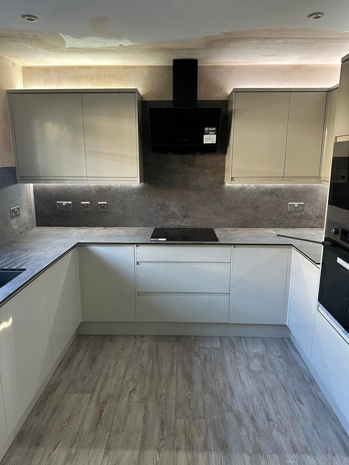 Front view of the fitted kitchen with illuminated cabinetry, dark splashback and hob