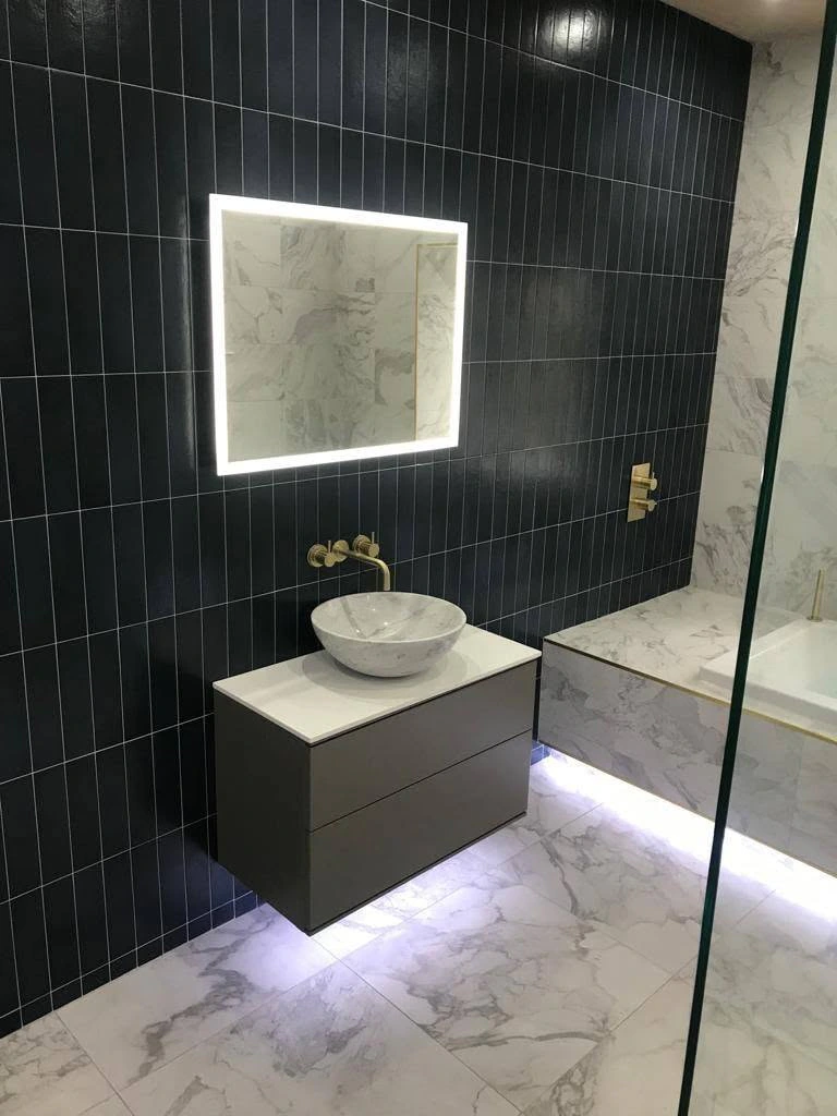 Marble and black tiled shower room with floating vanity, illuminated mirror and warm brass fittings