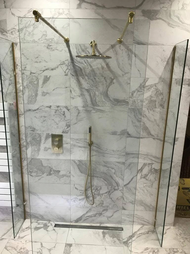 Head-on view of a marble shower with warm brass fittings