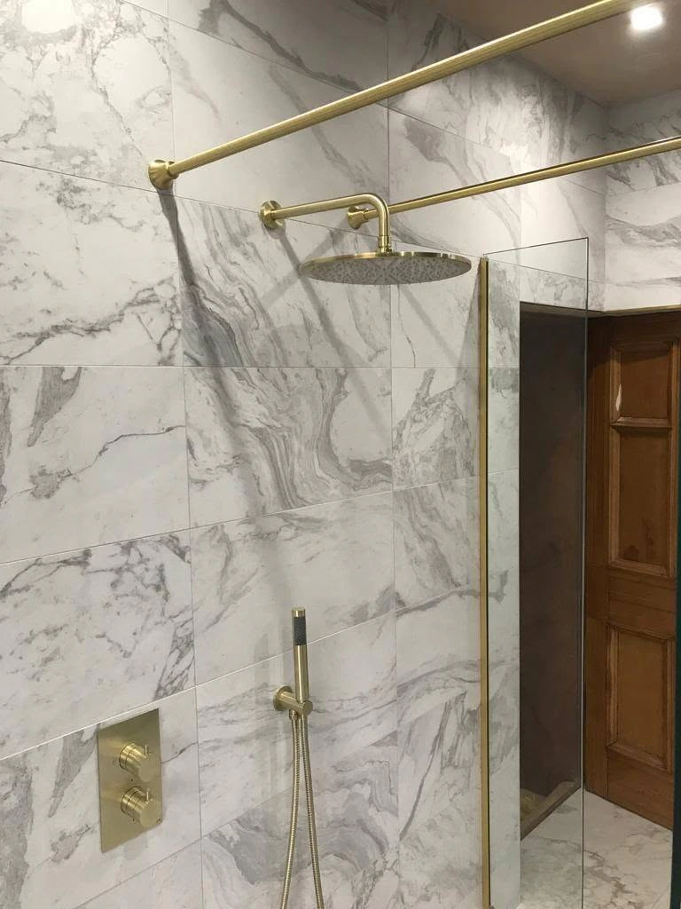 Brass rainfall and handheld shower fittings against marble-effect wall tiles