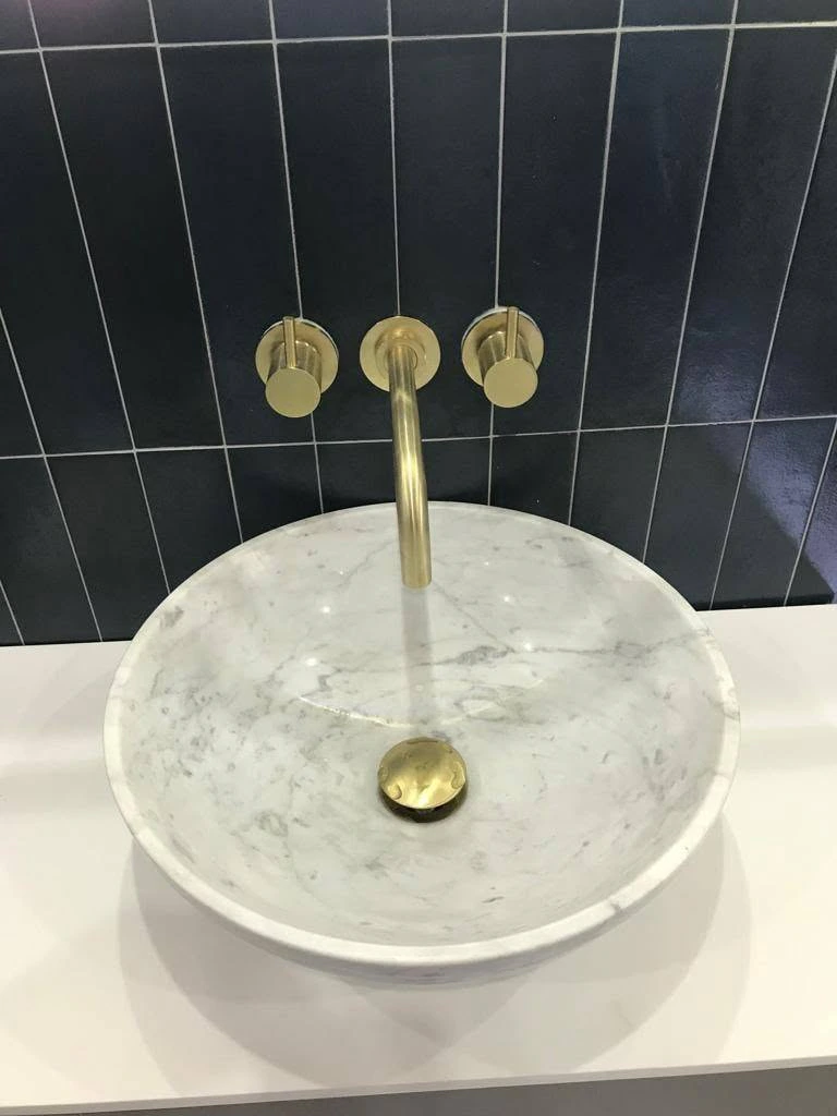 Marble basin with wall-mounted brass tap against black vertical tiles