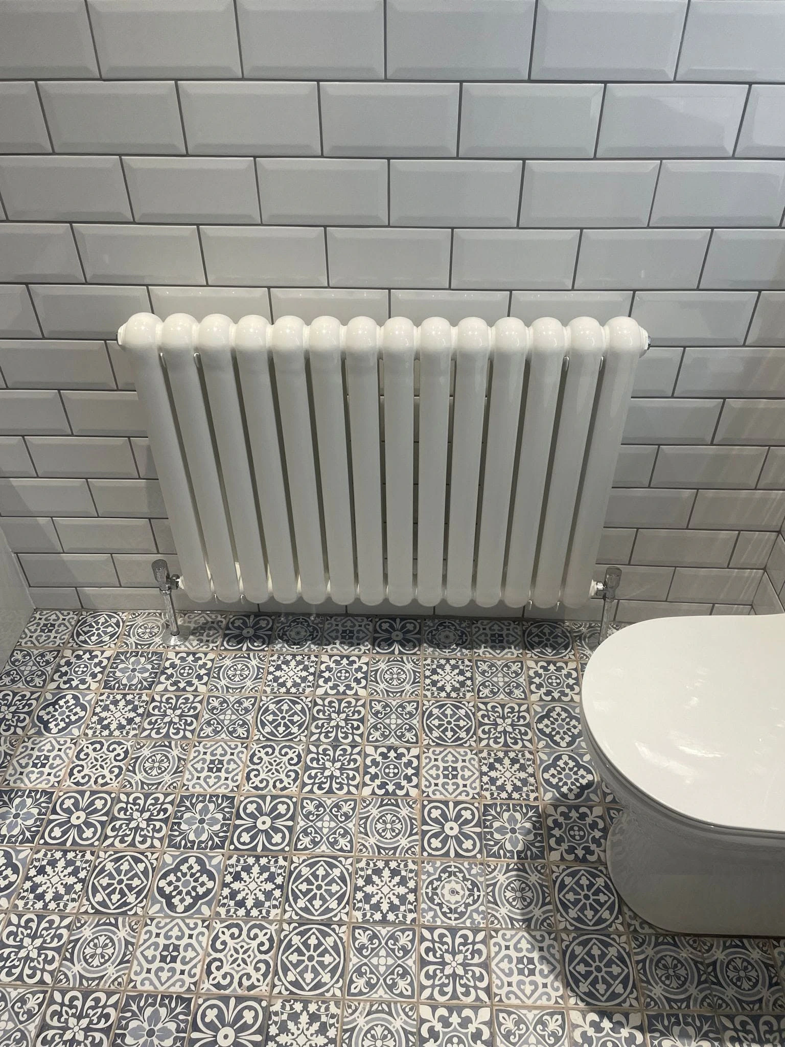 White traditional radiator against bevelled wall tiles and patterned bathroom flooring